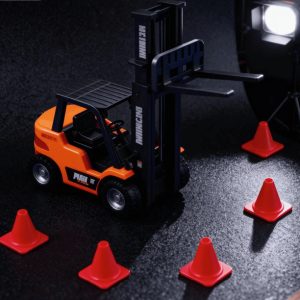 Miniature orange and black toy forklift with red traffic cones on a dark surface, illuminated by a studio light.