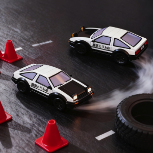 Two Initial D Fujiwara Tofu Shop AE86 toy cars drifting around red cones and a loose tire on a dark road.