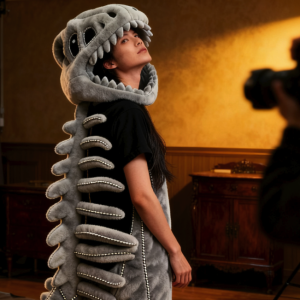 Person in a gray dinosaur skeleton costume posing for a photoshoot with a vintage gramophone.