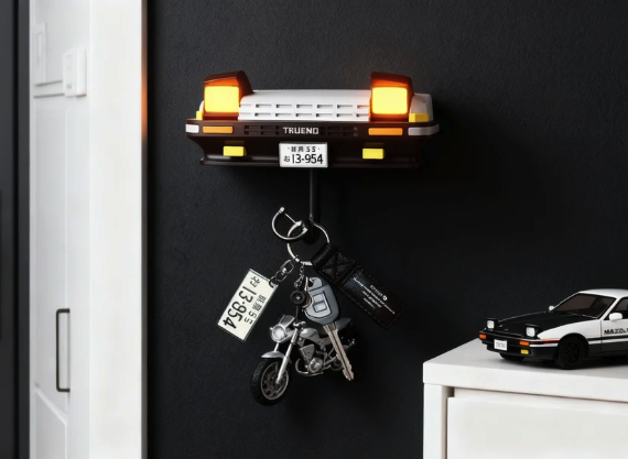 Toyota AE86 Trueno car front key holder with illuminated pop-up headlights, holding keys, next to a Mazda RX-7 model car.