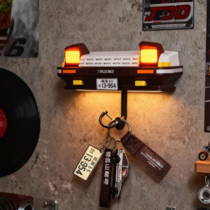 Illuminated Toyota AE86 Trueno key holder with pop-up headlights, surrounded by Initial D posters and car enthusiast decor.