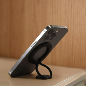 Silver iPhone with black magnetic ring phone stand as kickstand on a beige surface.