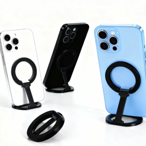 Three iPhones in silver, black, and light blue standing upright with black magnetic ring kickstands attached, plus one loose kickstand.
